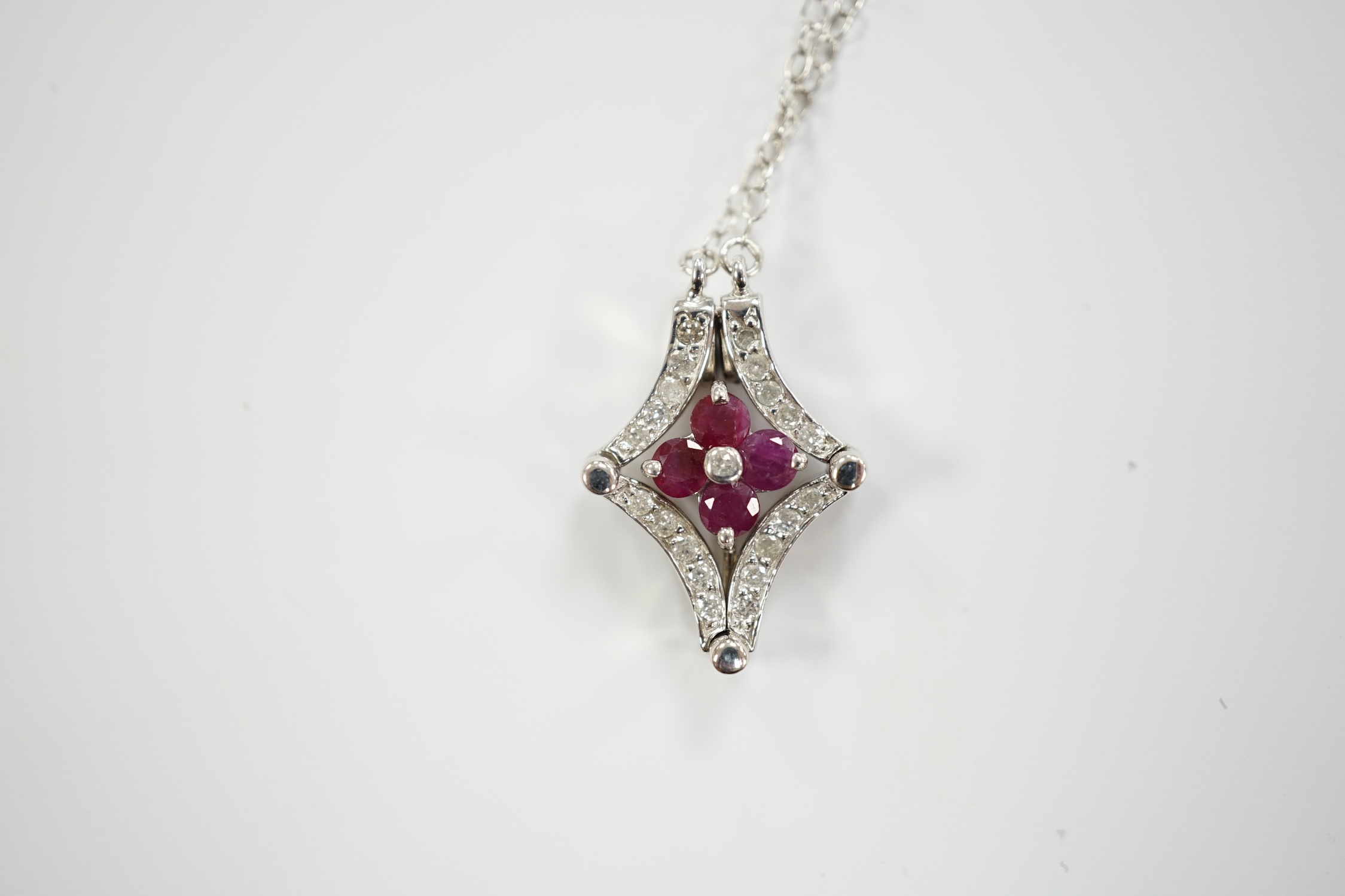 A modern 14ct white gold, ruby and diamond cluster set metamorphic pendant, 21mm, on a 14k white metal fine link chain, 38cm, gross weight 3.8 grams.